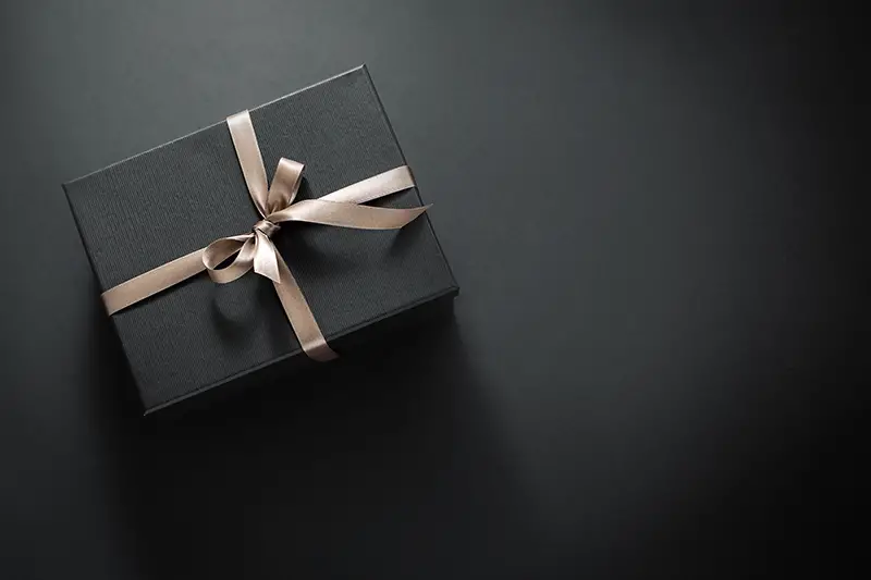 One gift wrapped in dark black paper with luxury bow on dark background.