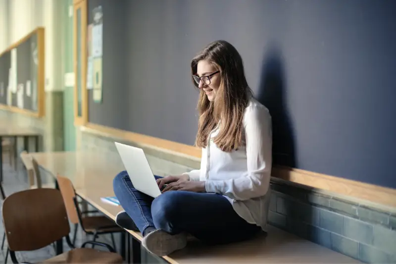 Young female student sitting on table while using Macbook