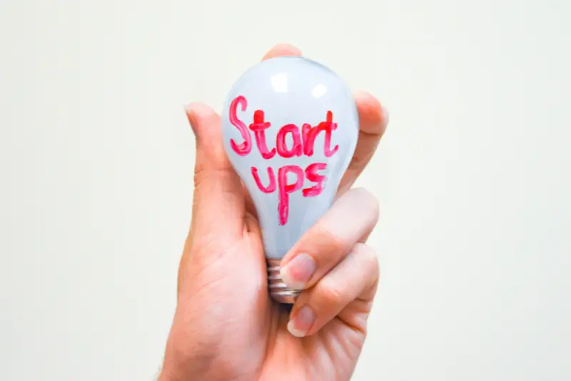 Startups word written on white bulb on person hand