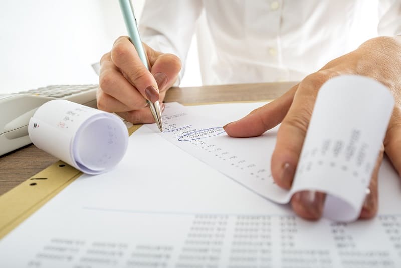 Closeup of female accountant looking through the receipts while working on a report.