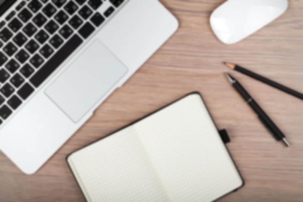 Laptop on a desk next to note pad, pens