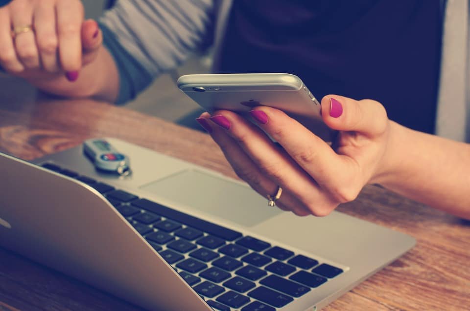 PErson holding mobile phone above laptop computer