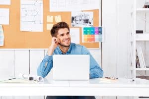 Happy young handsome businessman sitting at his workplace in office and talking on the mobile phone