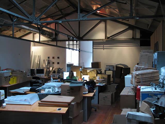 Person sat a desk in an office crowded with lots of boxes