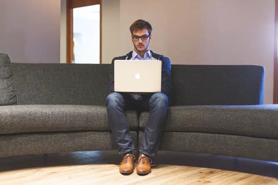 Young man sitting on grey sofa with laptop on knees