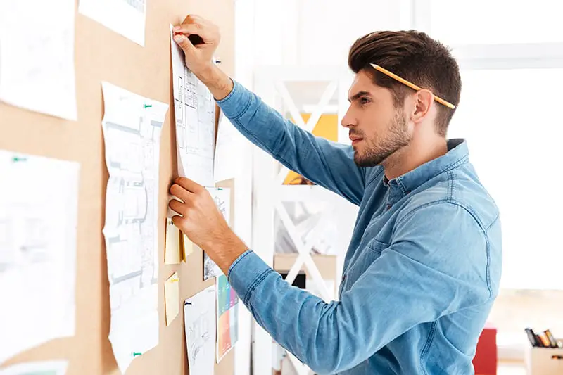 Serious casual businessman posting business plan at the office board while sitting at the desk