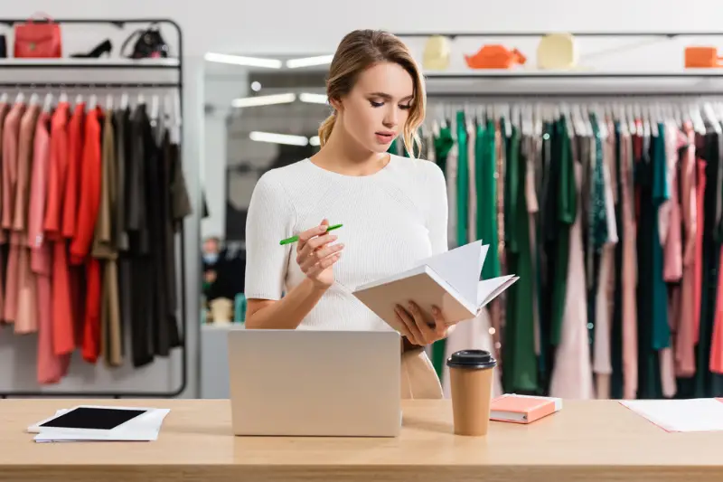 Seller working with pen and notebook near devices and papercup in a showroom