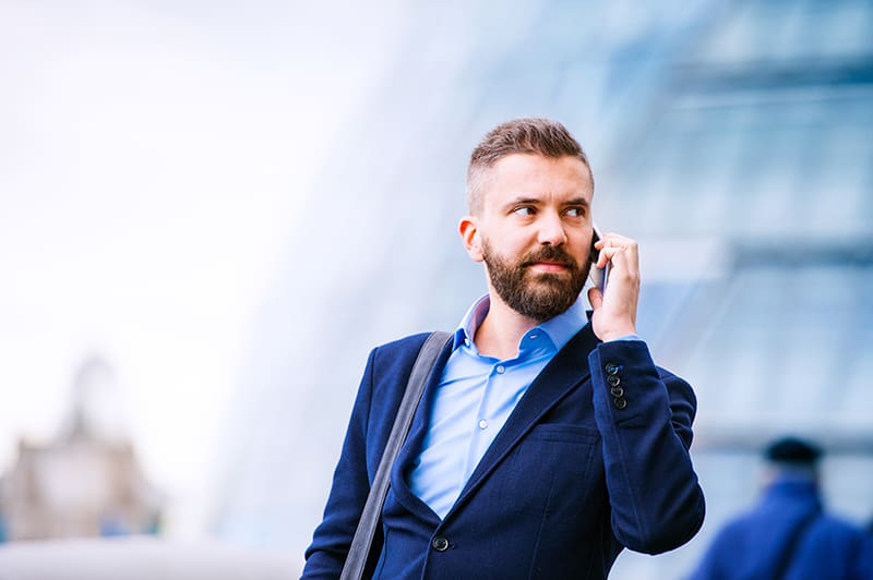 Hipster manager holding a smart phone, making a phone call, City Hall, London