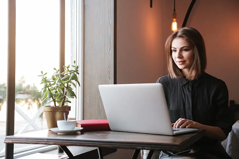 Image of pretty young lady sitting at the table in cafe and looking at laptop computer.