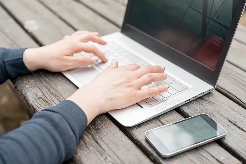 person typing on laptop mobile phone wooden table