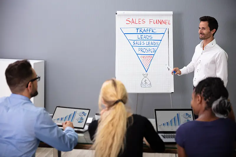 Young Smiling Businessman Explaining Sales Funnel Diagram To His Colleagues In Meeting