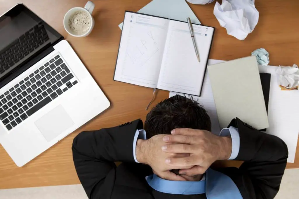 man holding his head at a cluttered desk