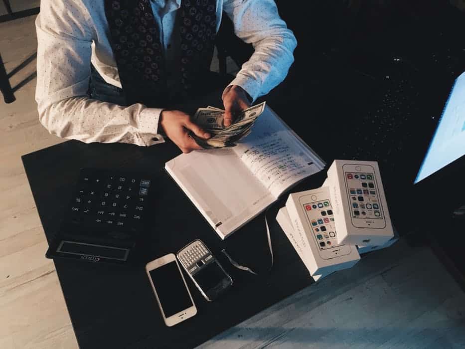man with dollars in hand desk book mobile phone calculator