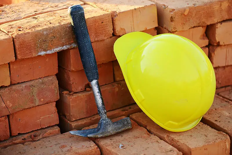 Under construction, helmet with hammer and bricks for building site