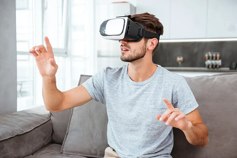 Photo of young man wearing virtual reality device while sitting on sofa