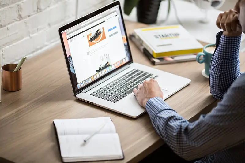 A man wearing blue longsleeve polo working in front of his laptop