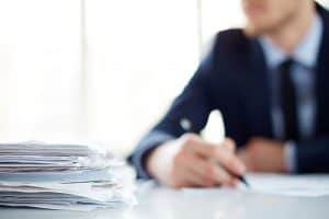 Stack of documents at workplace and male employee on background