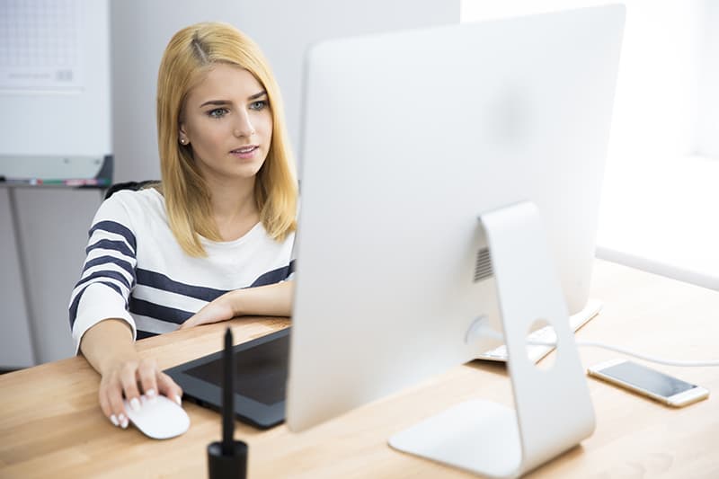 Casual young female photo editor working on computer in office