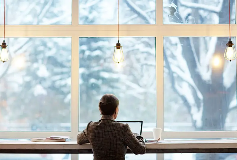 Back view of elegant-looking entrepreneur writing email to her business partner while enjoying delicious coffee and picturesque view of cyber cafe