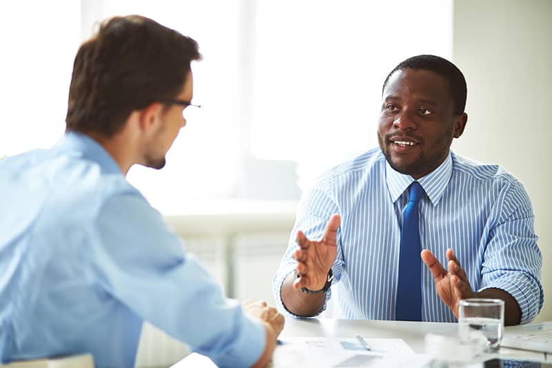 Image of two young businessmen interacting at meeting in office