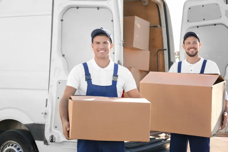 Delivery men with moving boxes near removal van