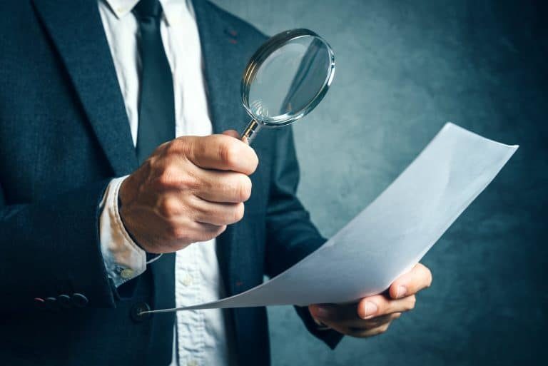 Man in suit looking at document through magnifying glass