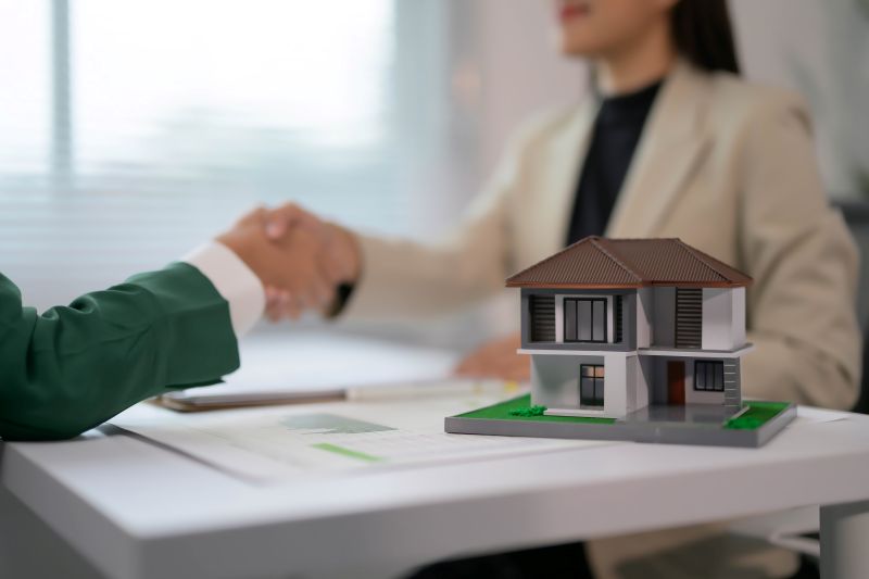 Real Estate Agent Shaking Hands with Client Over House Model on Desk in Modern Office Setting
