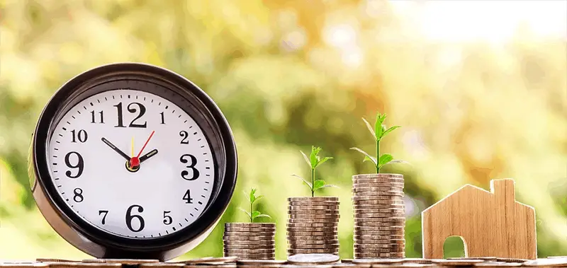 Clock next to stacks of coins with plants on top, growing investment