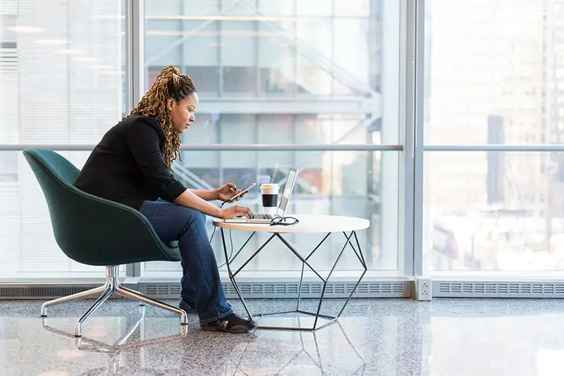 woman sitting on chair at a table using mobile phone and laptop computer