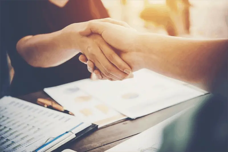 two people shaking hands across a table covered with documents