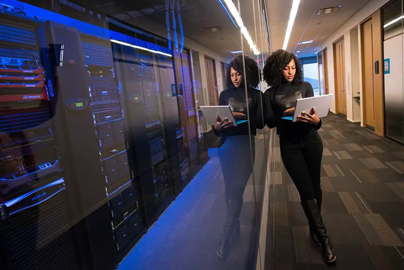 woman leaning again glass wall holding computer 