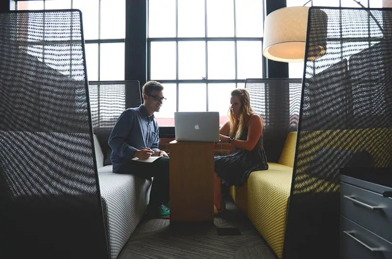 man and lady sitting in a booth looking at laptop computer