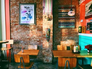 restaurant interior - two square brown wooden dining tables near brown brick wall