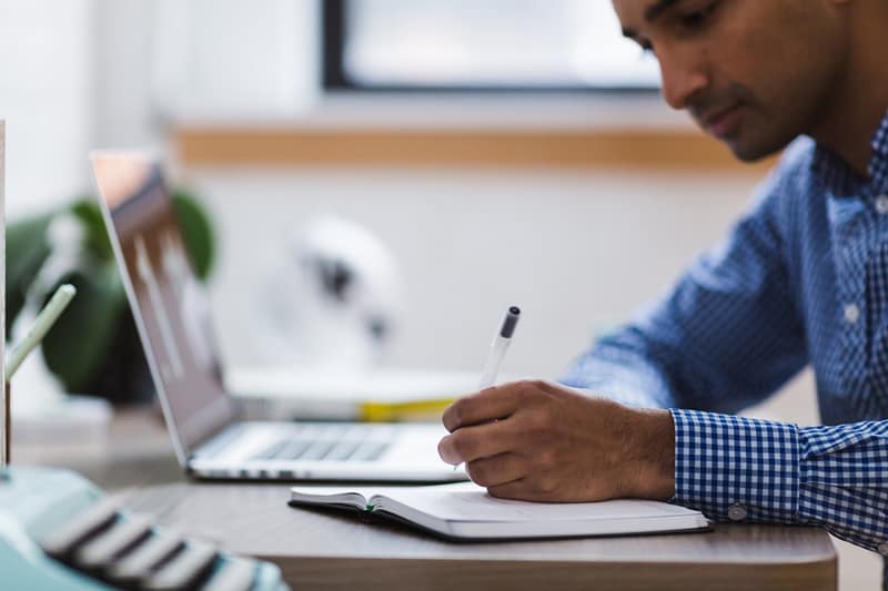 person writing at a desk next to open laptop - studying for Masters in International business