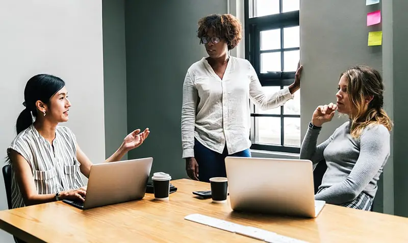 Team communication - three woment talking near laptop on desk in room