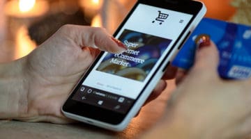 person using black and white smartphone and holding blue credit card for eCommerce checkout process