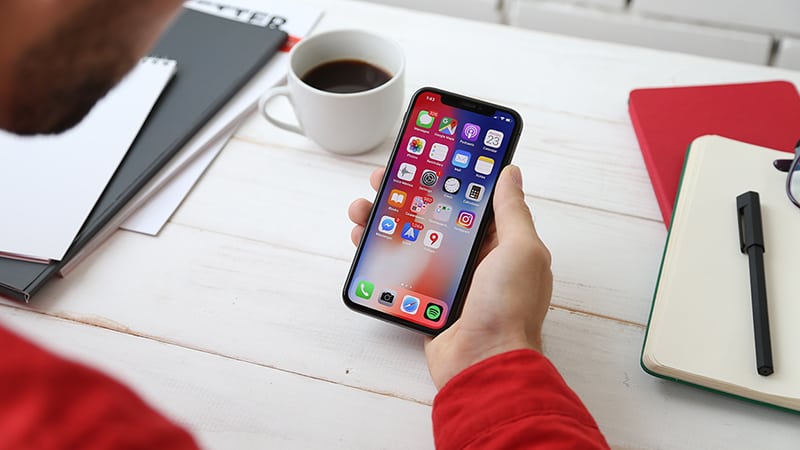 person holding space gray iPhone X with mobile app icons on screen