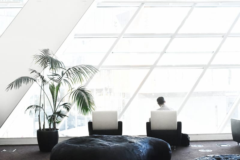 man in white dress shirt sitting on black and white tube chair next to office windows