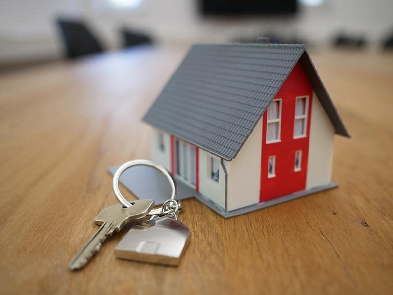 Property Management white and red wooden house miniature on brown table next to a property key
