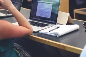 Person sitting in front of laptop computer with notebook and pen by the side