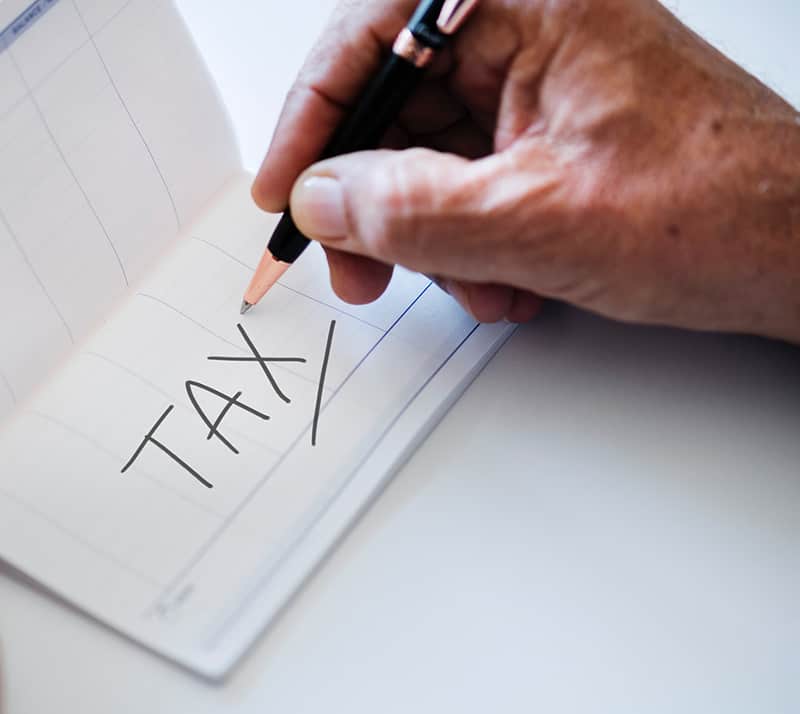 Person holding a black pen – tax written in notebook