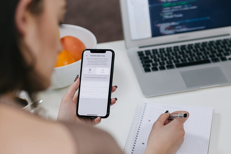 person holding smartphone using mobile app and making notes