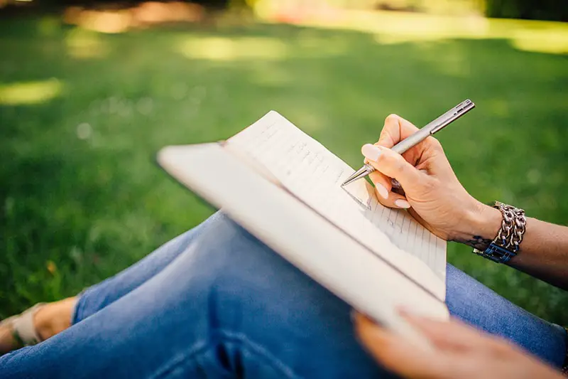 person sitting on grass writing in a book 