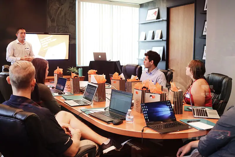 presentation delivery in front of people sitting beside table with laptop computers