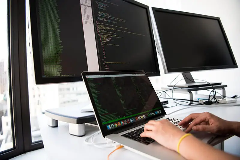 IT personnel typing on laptop connected to dual monitors.