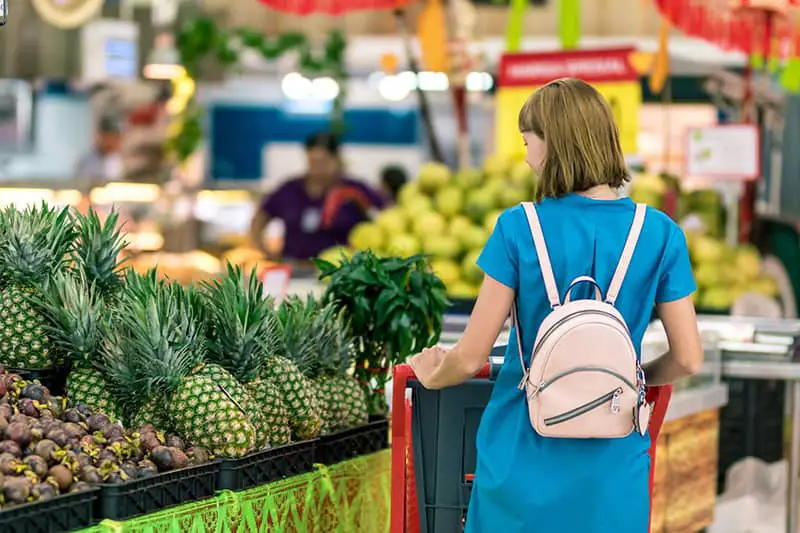 woman pushing trolley pas produce displays of pineapple and fruits