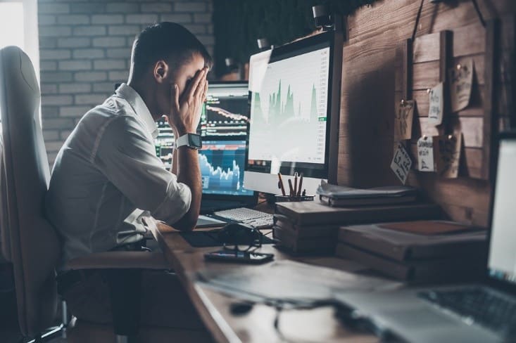 Man with head in hands in front of computer monitor.