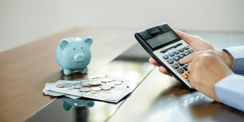 Man calculating her expenses on a notebook putting coin into piggy bank.