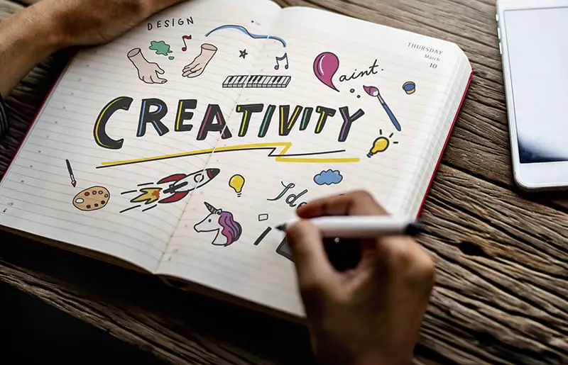  Person doodling pictures and the word “creativity” in a notebook. 