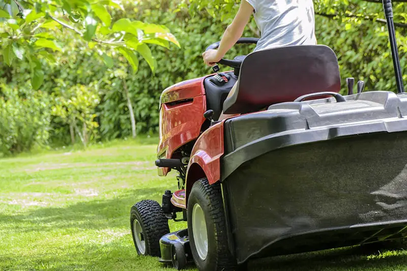 Person with lawn care business cutting grass on ride on lawn mower